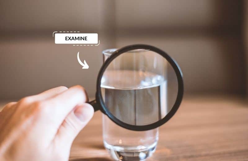 hand holding a magnifying glass onto water in a drinking glass