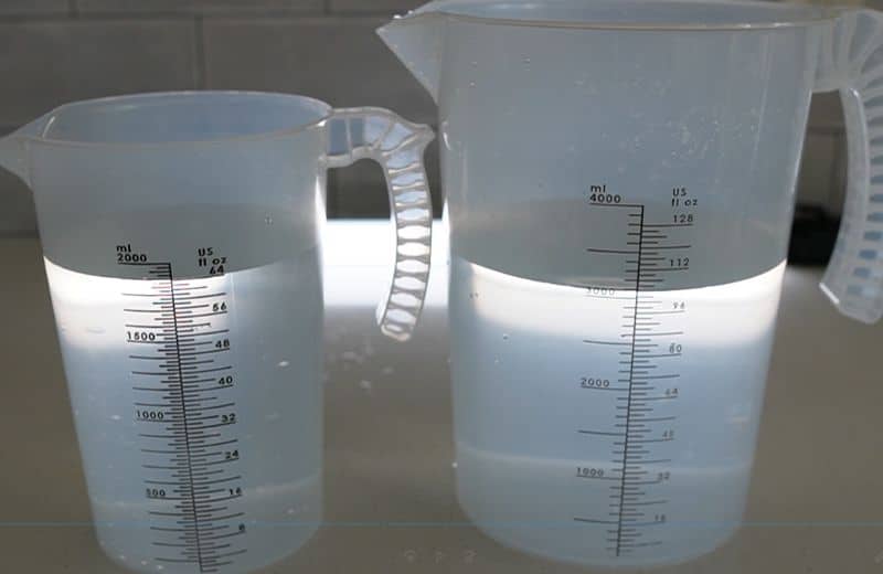 Two plastic measuring pitchers filled with cloudy, milky water sitting side by side; both containers display ounce markings