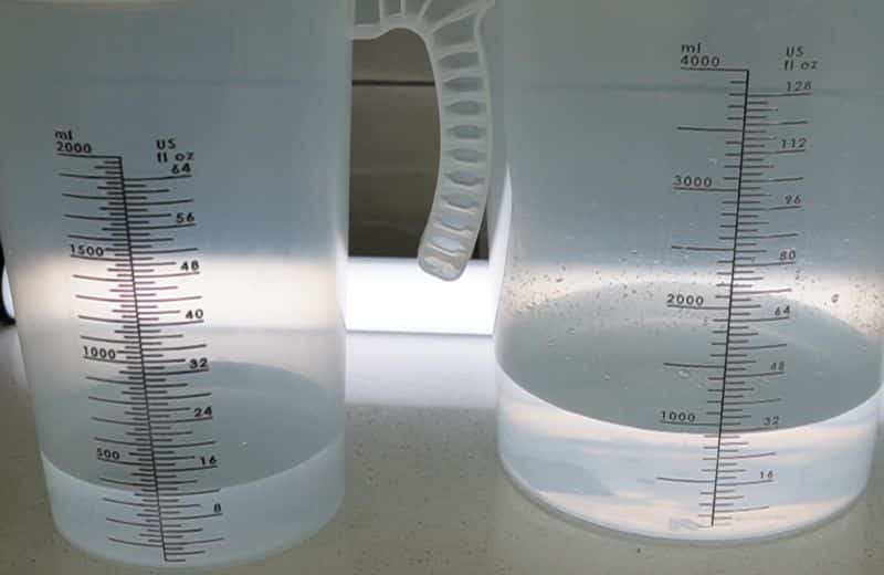 Two translucent measuring pitchers on a countertop, each partially filled with cloudy water with measurement markings visible.