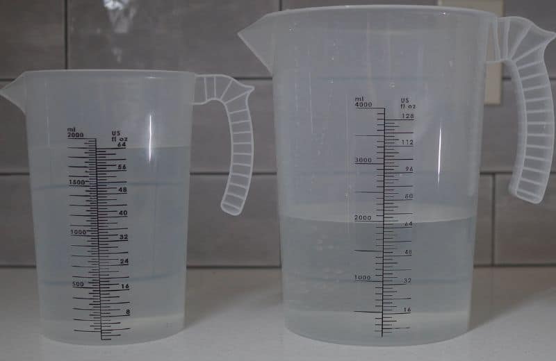Two transparent plastic measuring jugs sit side by side on a countertop. The left jug shows the Cloud RO purified water at 64 oz. The right jug shows the Cloud RO waste water, at 66 oz.