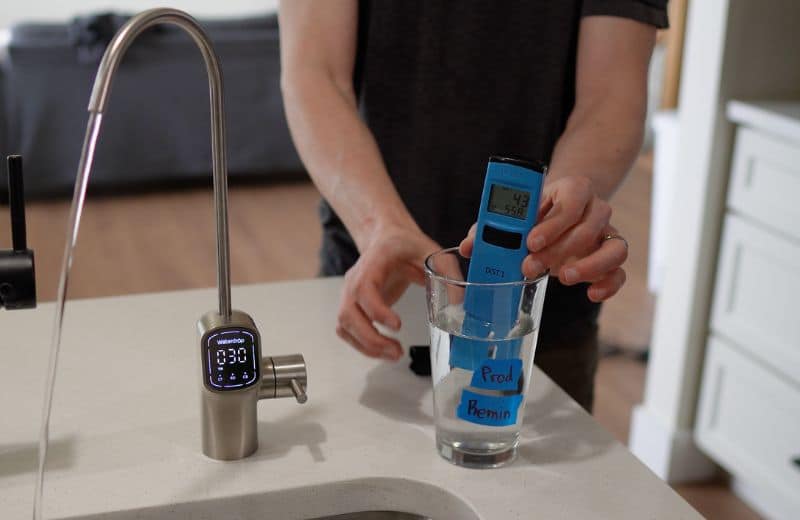 Waterdrop G3 P800 TDS reading Post Remin Waterdrop G3P800 reverse osmosis system dispensing filtered water while a blue TDS meter measures dissolved solids in a glass labeled product remineralized water.