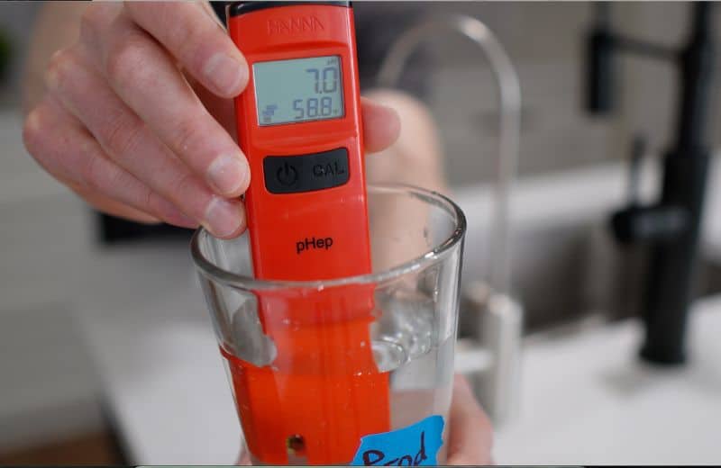 Waterdrop G3P800 pH Level Close-up of a red pH meter testing filtered water from the Waterdrop G3P800 reverse osmosis system, displaying a neutral pH reading in a glass sample.