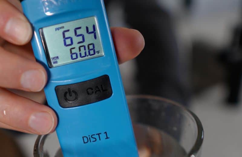 KindWater PRO pre filtration TDS reading A close-up of a blue handheld meter held above a glass of water shows “654 ppm” and “60.8°F” on the display. The device is used to measure KIND WATER PRO RO product water quality.
