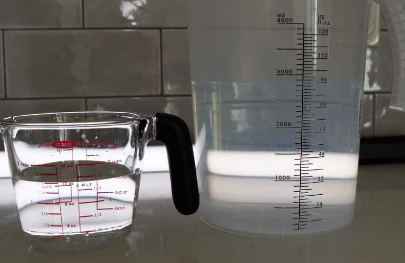 US Water Made RO efficiency ratio A translucent plastic measuring pitcher and glass pitcher on a countertop, each partially filled with water with measurement markings visible showing US Water Made RO efficiency ratio
