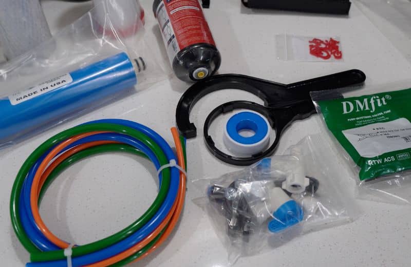 US Water Made RO system installation kit US Water Made RO system installation kit with color-coded tubing, RO membrane, fittings, tank wrench, and connection accessories laid out on a countertop.