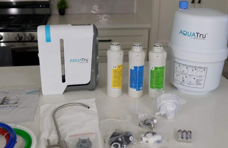 AquaTru Under Sink 2nd Gen Complete Kit A full set of filtration components—including the main unit, storage tank, color‑coded filters, tubing, and faucet hardware are laid out on a kitchen counter as part of the Aquatru Under Sink RO 2nd gen installation kit.