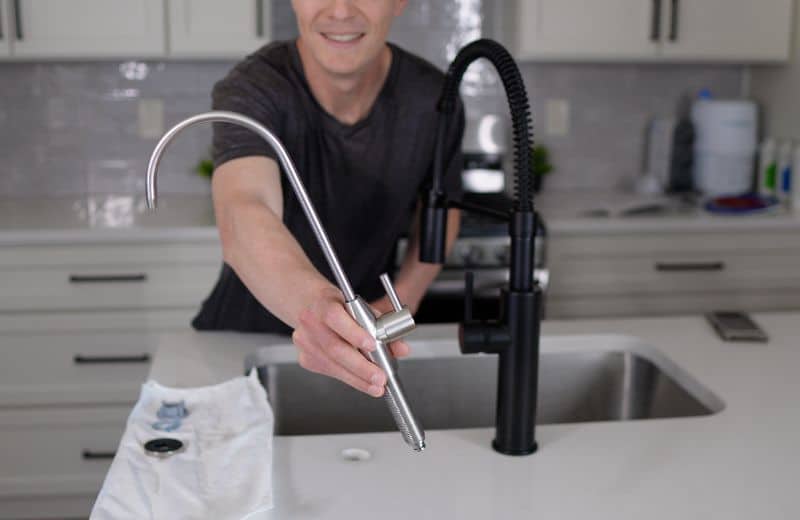 AquaTru Under Sink 2nd Gen Faucet Brian holds a metallic faucet fixture near a kitchen sink, preparing the dedicated purified‑water faucet used with the Aquatru Under Sink RO 2nd gen system.