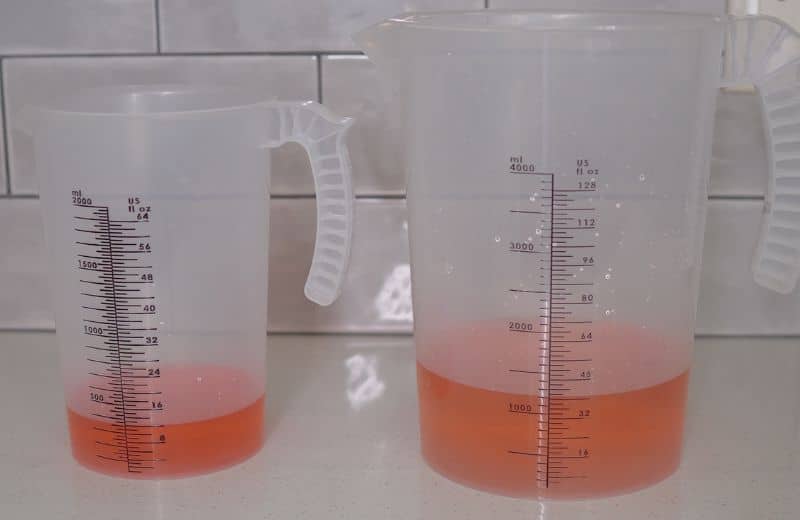 AquaTru Under Sink 2nd Gen Wastewater Collected Two transparent measuring jugs containing small amounts of red liquid are shown side by side, used for testing water output volumes during Aquatru Under Sink RO 2nd gen system calibration.
